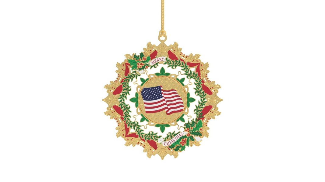 Christmas ornament with an American flag in the center, surrounded by a festive wreath design featuring red, green, and gold elements, with holly berries and leaves. The text "Merry Christmas" is displayed at the top and bottom of the ornament.