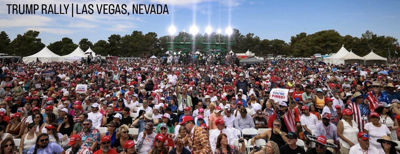 A large crowd of people, many wearing red "MAGA" hats, attending a Trump rally in Las Vegas, Nevada, with signs reading "You're Fired!" and various tents and trees in the background.