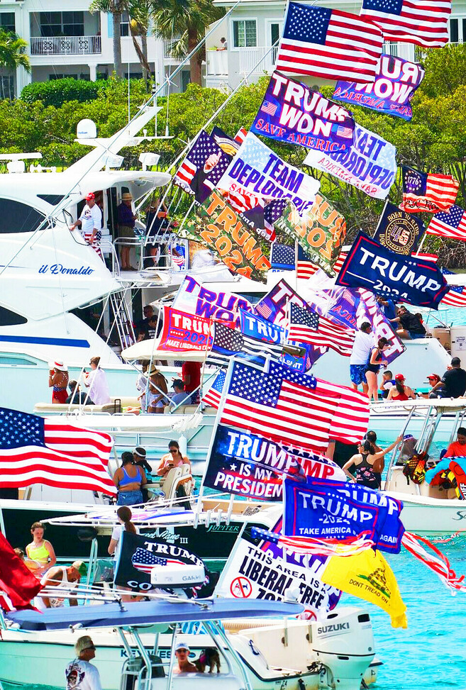 Boats in a parade decorated with American flags, pro-Trump banners, and various political slogans, including "Trump Won," "Team Deplorable," and "Trump 2024," with people on board enjoying the event.