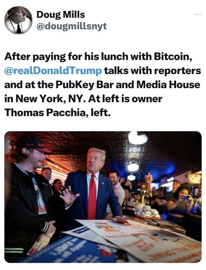 Doug Mills tweet: “After paying for his lunch with Bitcoin, @realDonaldTrump talks with reporters and at the PubKey Bar and Media House in New York, NY. At left is owner Thomas Pacchia, left.” A man in a suit converses with another man in casual attire inside a crowded bar with onlookers and phones in the background.