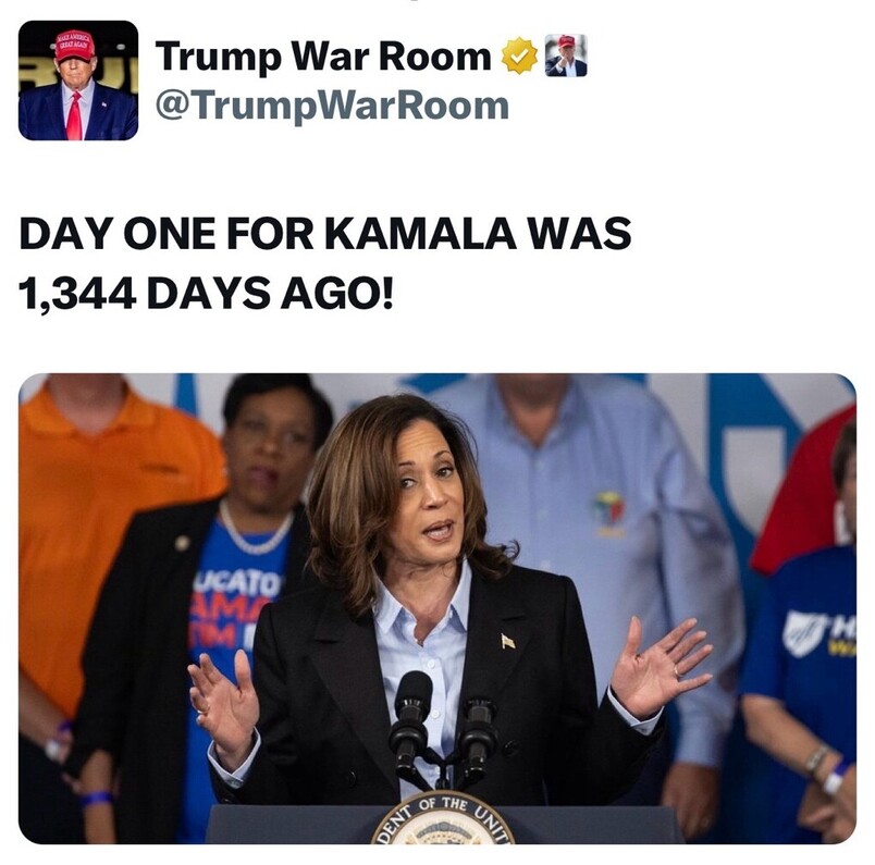 Twitter post from @TrumpWarRoom featuring a headline that reads, "DAY ONE FOR KAMALA WAS 1,344 DAYS AGO!" Below the headline, an image shows a woman speaking at a podium with microphones, wearing a dark blazer and a light-colored blouse. Behind her, several people are visible, some wearing shirts with visible text.