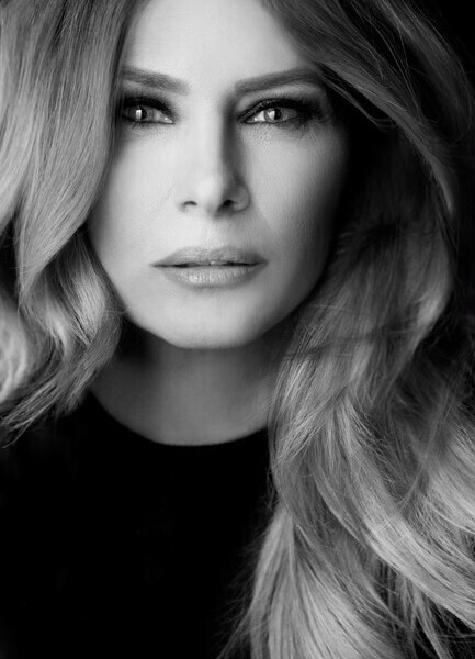 Black and white portrait of a woman with long, wavy hair, looking directly at the camera with an intense gaze. She has a calm and confident expression, and her facial features are highlighted by soft lighting.