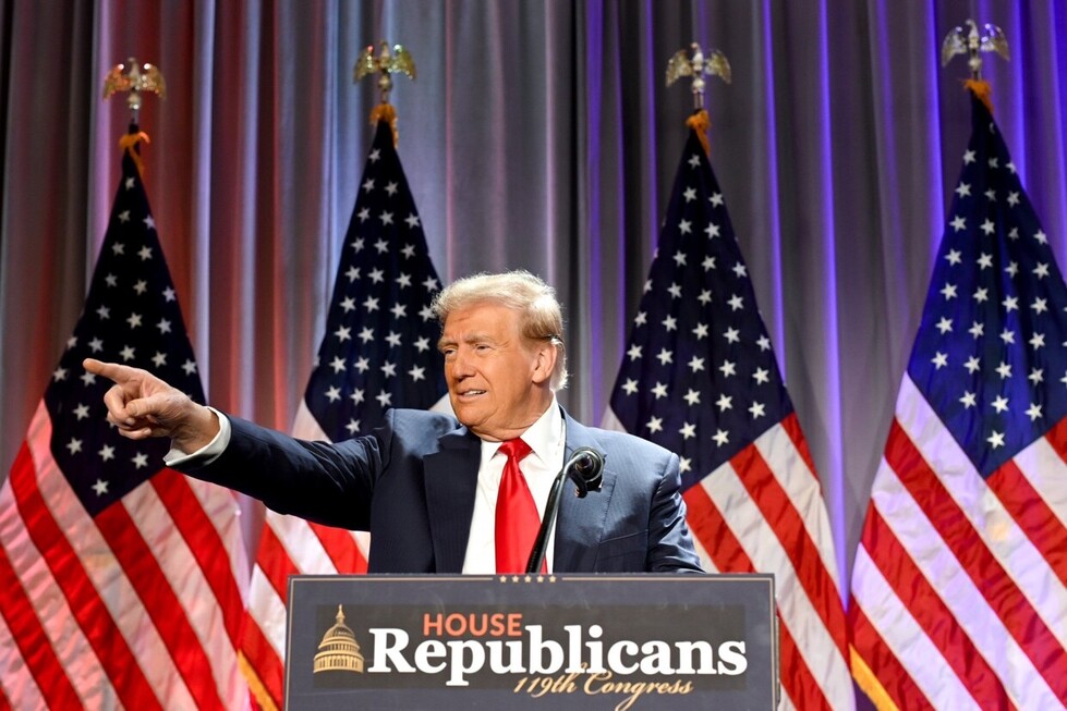 A man in a suit and red tie stands at a podium labeled "House Republicans 119th Congress," pointing and speaking, with five American flags in the background.