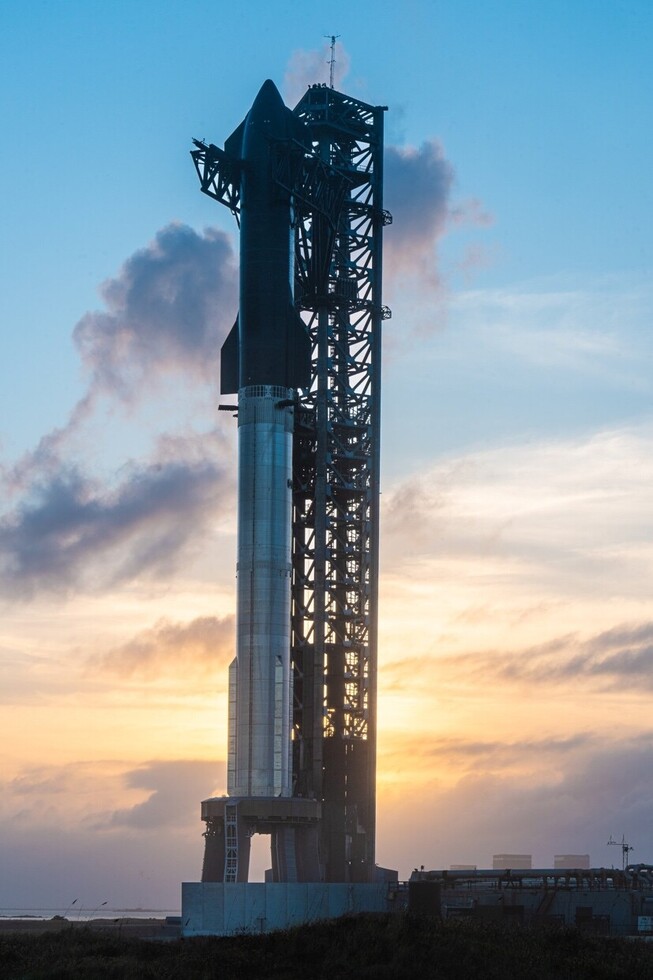 Rocket on launch pad at sunrise with clouds in the background.