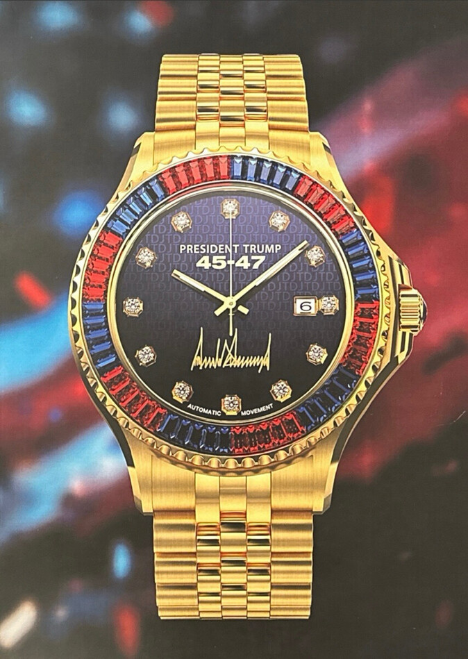Gold wristwatch with a gold band, featuring red and blue gemstones around the bezel. The watch face has diamond hour markers and displays the text "PRESIDENT TRUMP" and "4547" with a signature design. The backdrop includes blurred red and blue hues.